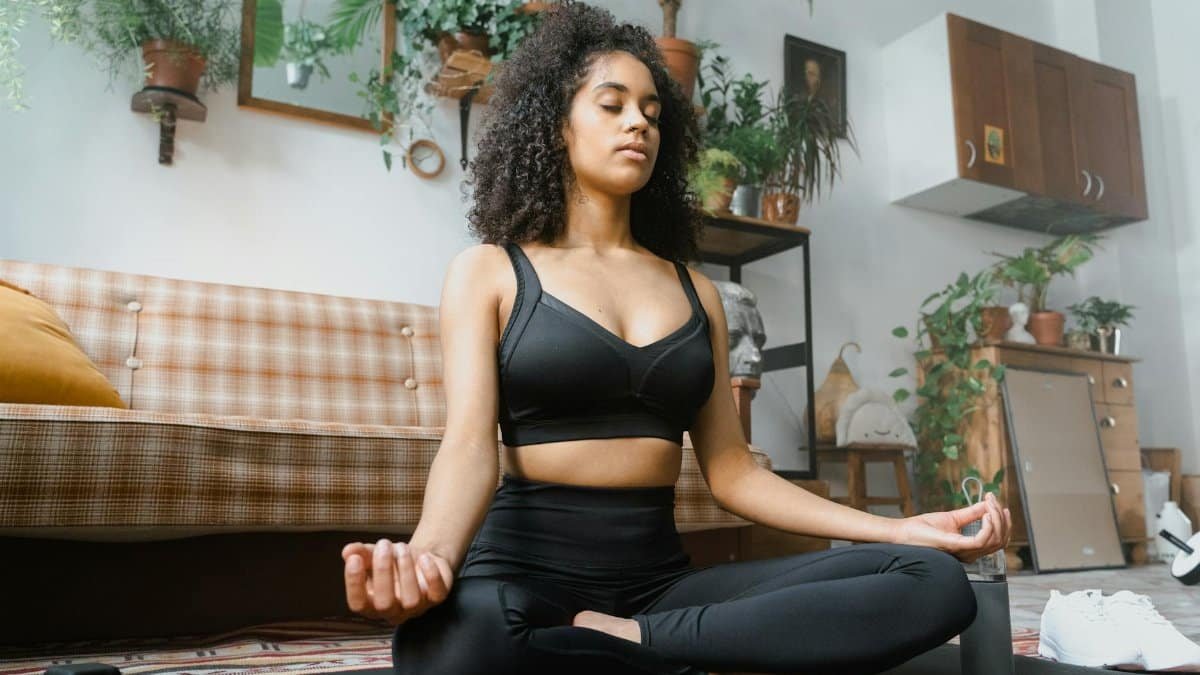 Calm woman in activewear meditating indoors, promoting a healthy lifestyle.