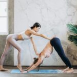 Yoga instructor guides student in downward dog pose during indoor session.