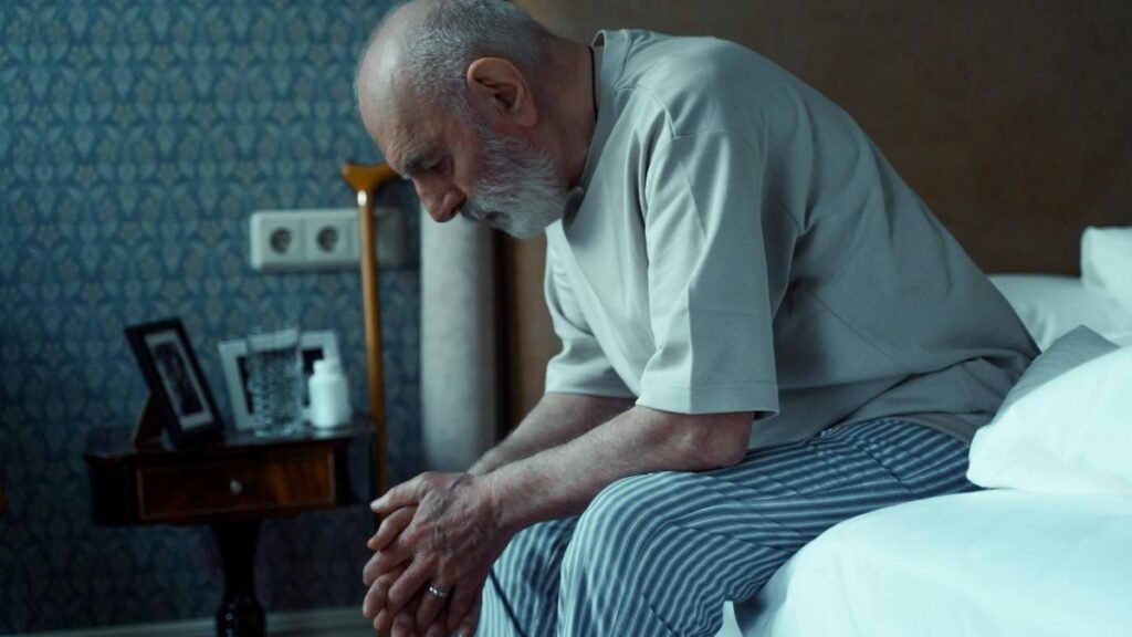An elderly man sits thoughtfully on a bed, conveying solitude and reflection.