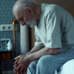 An elderly man sits thoughtfully on a bed, conveying solitude and reflection.