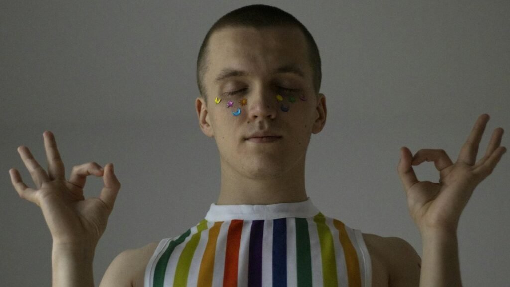 A person meditates indoors wearing a rainbow tank top, symbolizing LGBTQ pride.