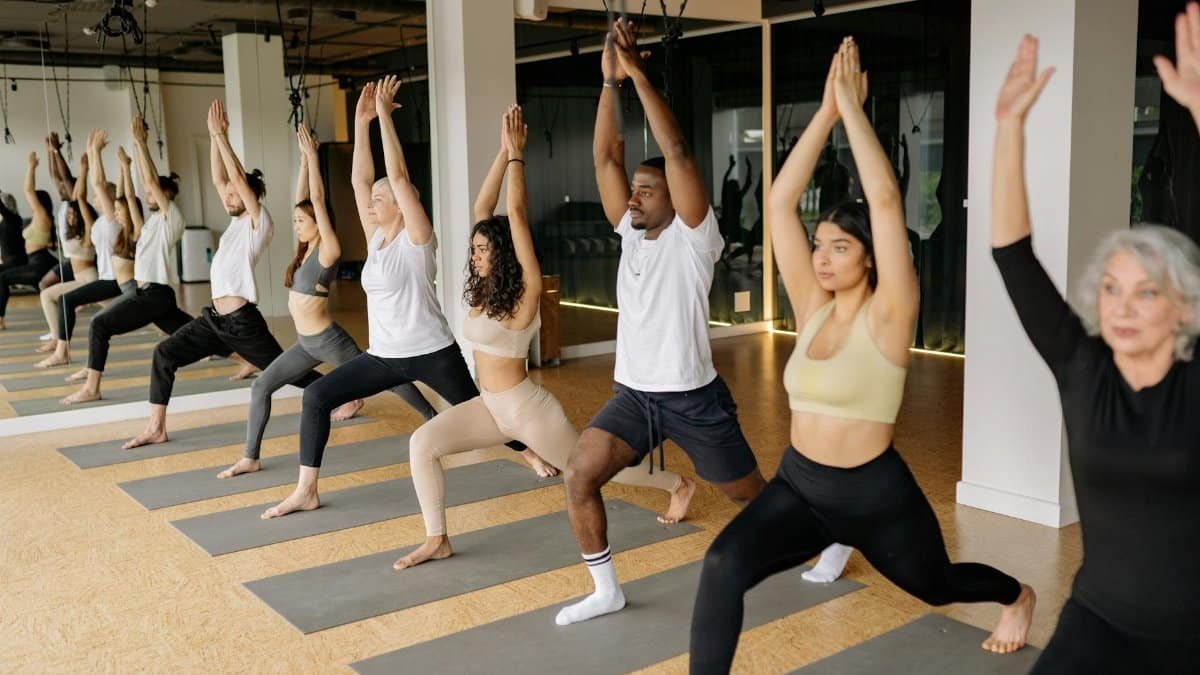 A diverse group practicing yoga with raised arms in an indoor studio setting.