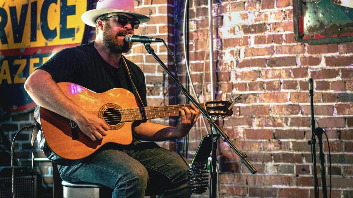 A musician plays acoustic guitar in a Nashville bar setting.