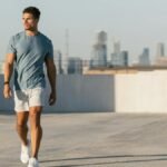 Young athletic man walking on rooftop with Austin skyline, wearing casual attire.