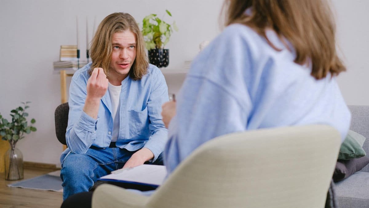 A young man in therapy, gesturing towards therapist in a comfortable setting.