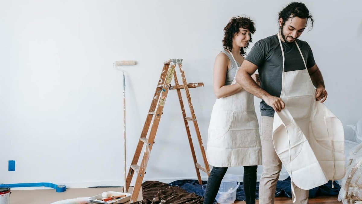 A couple in aprons getting ready to renovate their home, showing teamwork and joy.