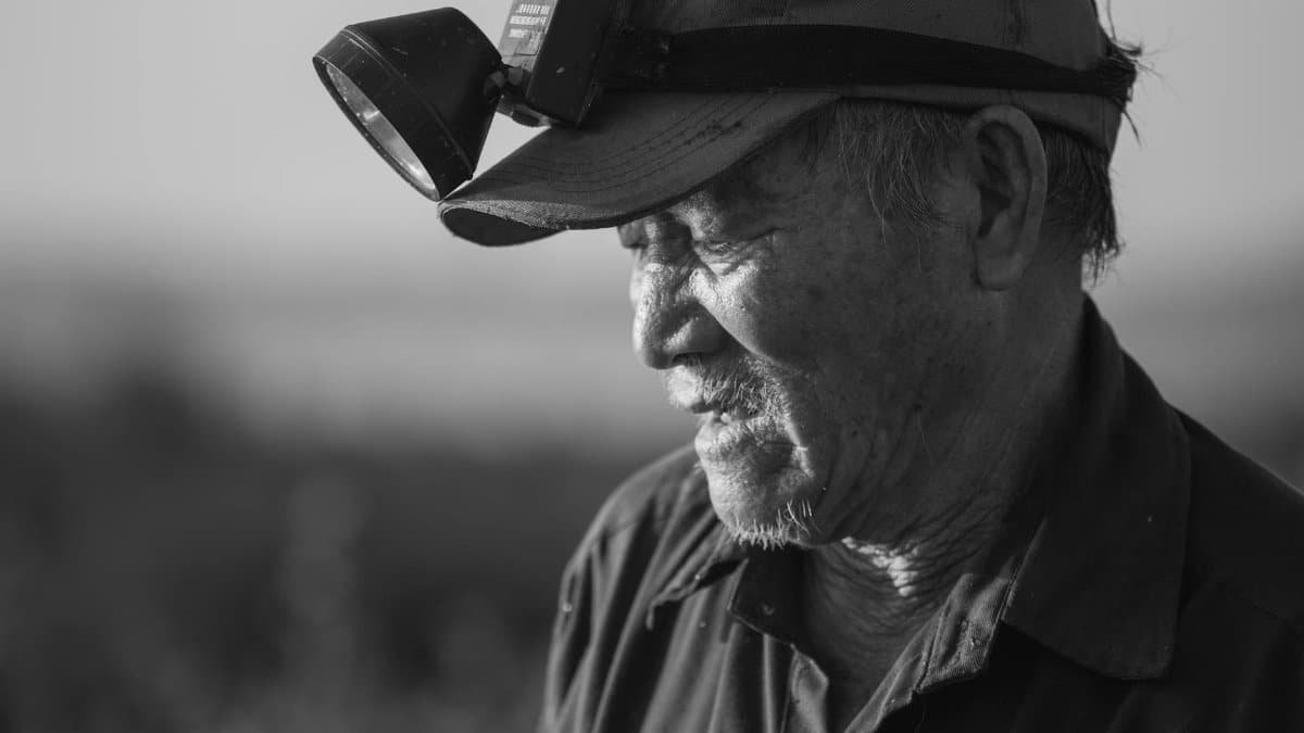 A senior man in monochrome wearing a cap and headlamp, exuding wisdom and experience.