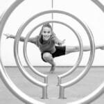 A woman striking a dynamic yoga pose framed by circular metal structures in black and white.