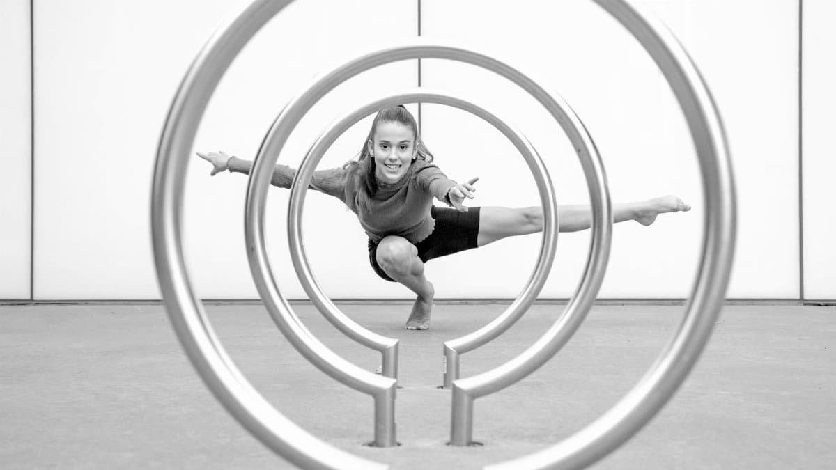 A woman striking a dynamic yoga pose framed by circular metal structures in black and white.