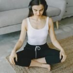 Woman meditating indoors on a rug with headphones, promoting relaxation and wellness.