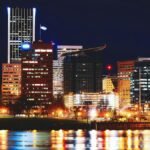 Vibrant Portland cityscape with reflections on the river and brightly lit skyscrapers at night.