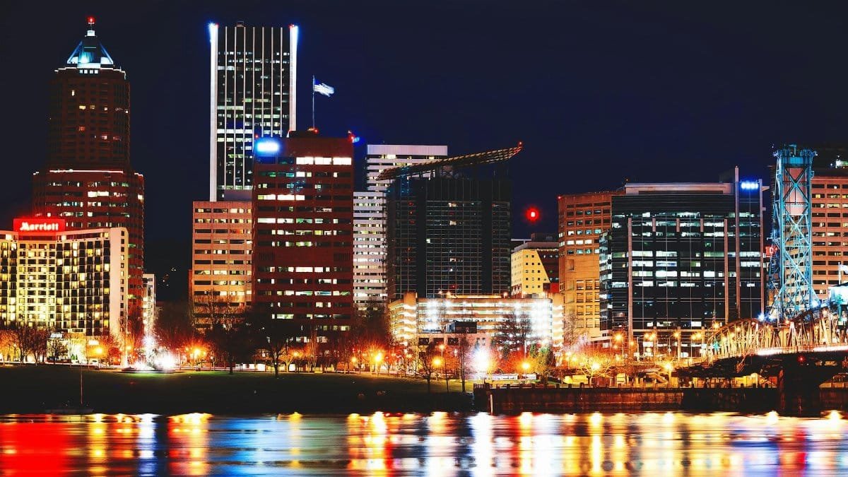 Vibrant Portland cityscape with reflections on the river and brightly lit skyscrapers at night.