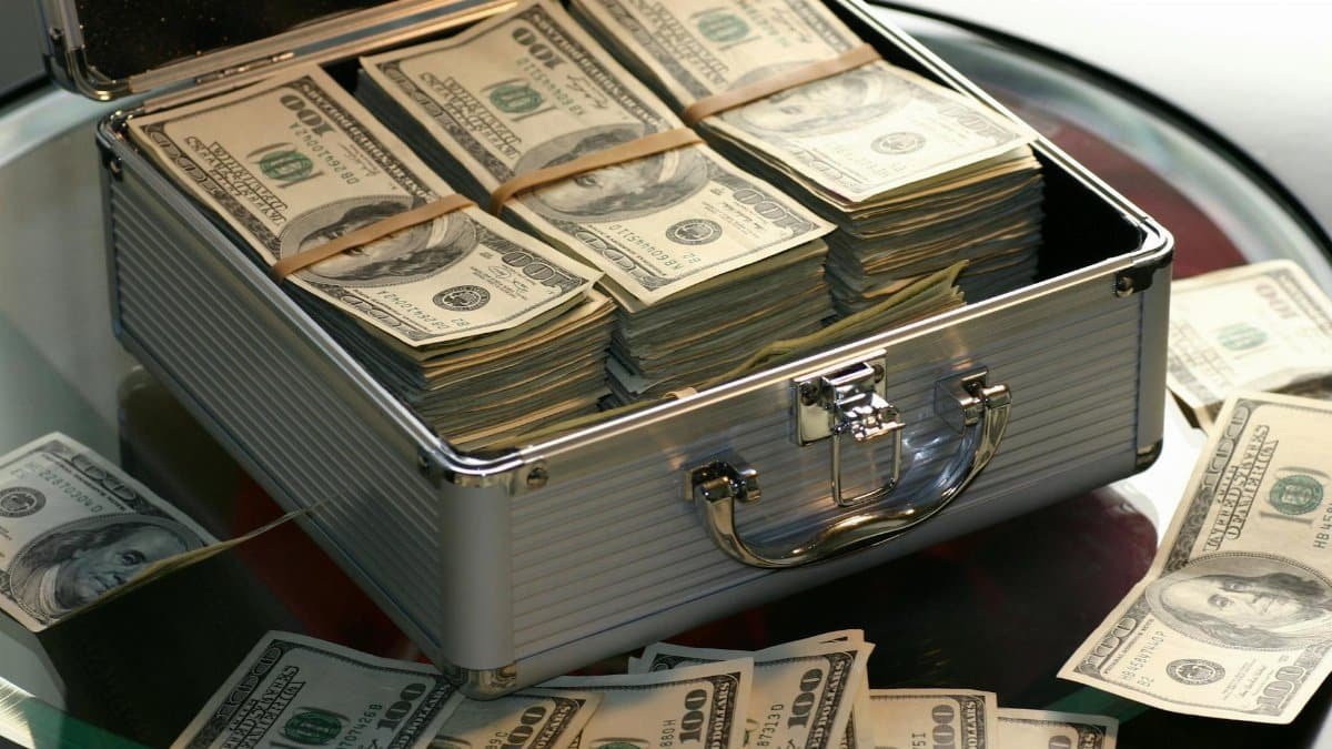 Open briefcase filled with stacks of hundred dollar bills on a glass table, representing wealth.