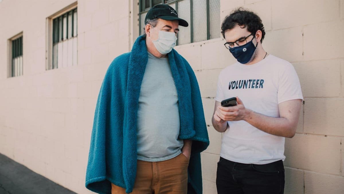 Two masked volunteers stand outside, collaborating on a smartphone project, enhancing community support.
