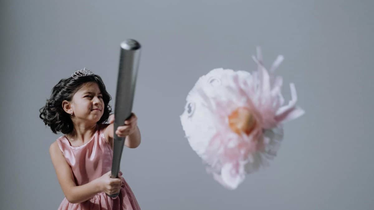 A young girl swings a baseball bat at a pinata in a studio shoot, capturing action and fun.