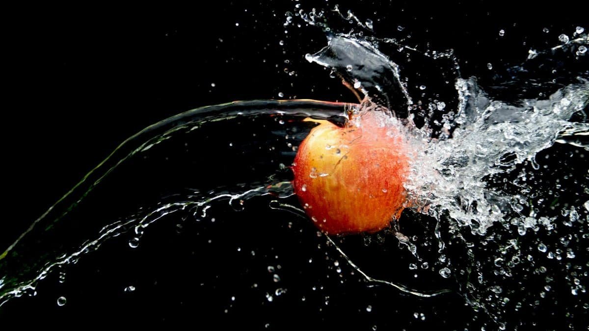 Dynamic close-up of an apple splashing through water with a black background. Perfect for creative advertising.