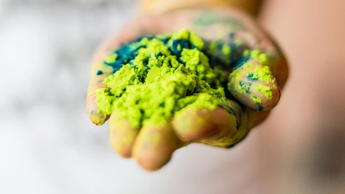 A close-up of a hand holding vibrant green and blue Holi powder, symbolizing festival celebration.