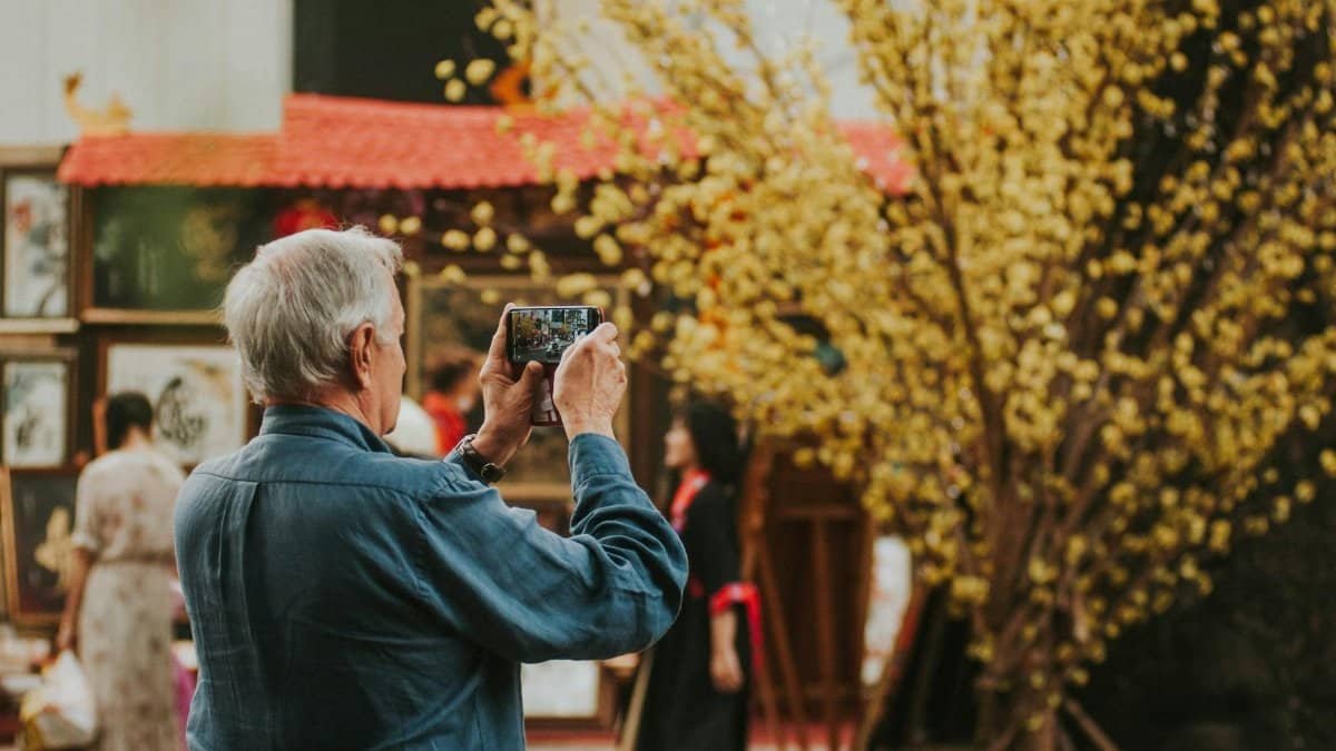 Elderly man takes a photo of outdoor art display with smartphone in spring.