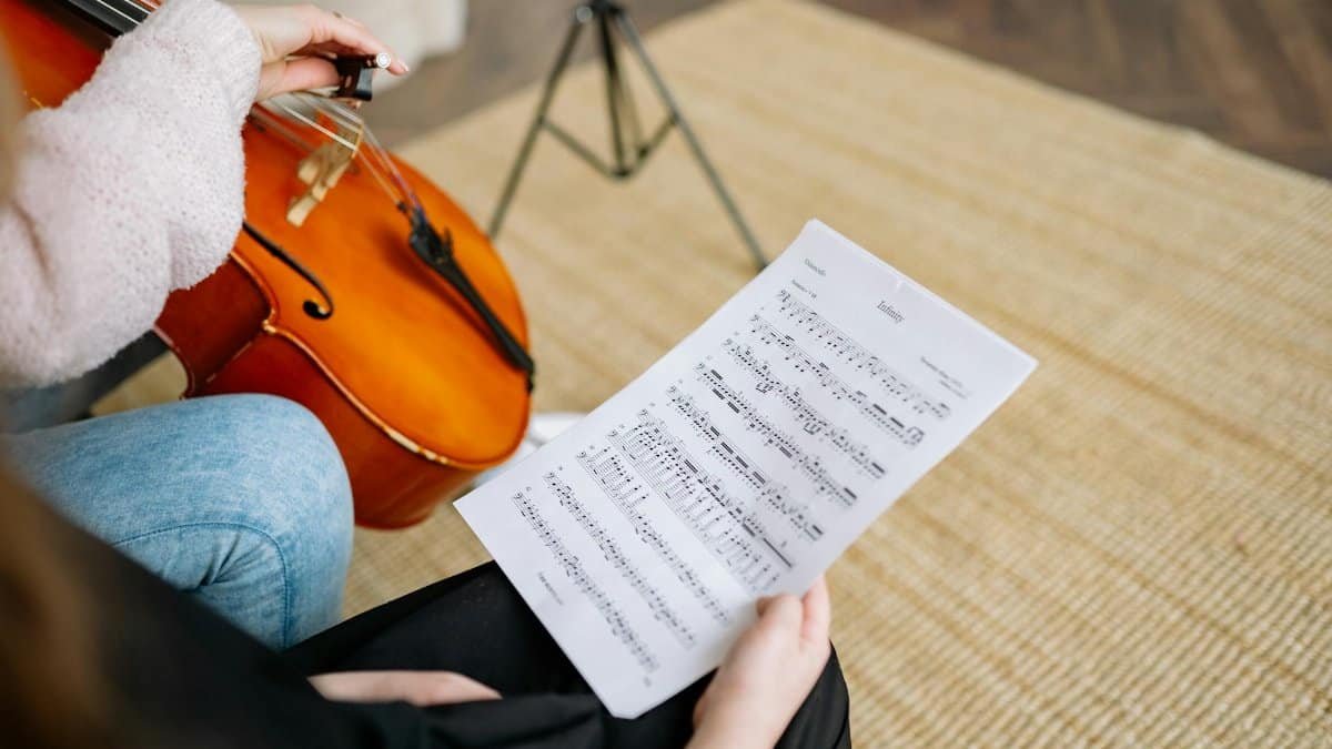 Detailed close-up of hands playing cello and holding music sheet during a lesson.