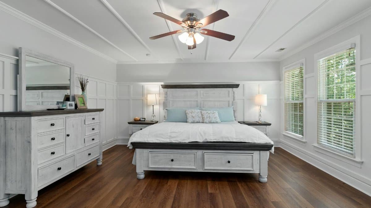 Cozy modern bedroom with white decor and wooden flooring, featuring ample natural light.
