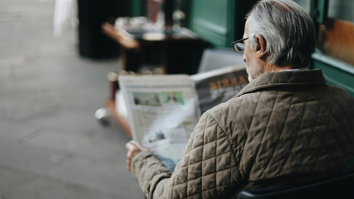 Elderly man reading a newspaper in an outdoor cafe setting, enjoying a peaceful moment.