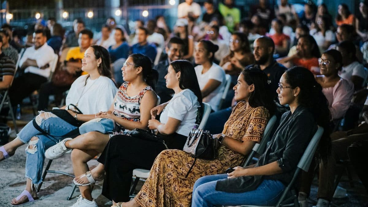 A diverse group of adults attentively watching an outdoor event during the evening with ambient lighting.
