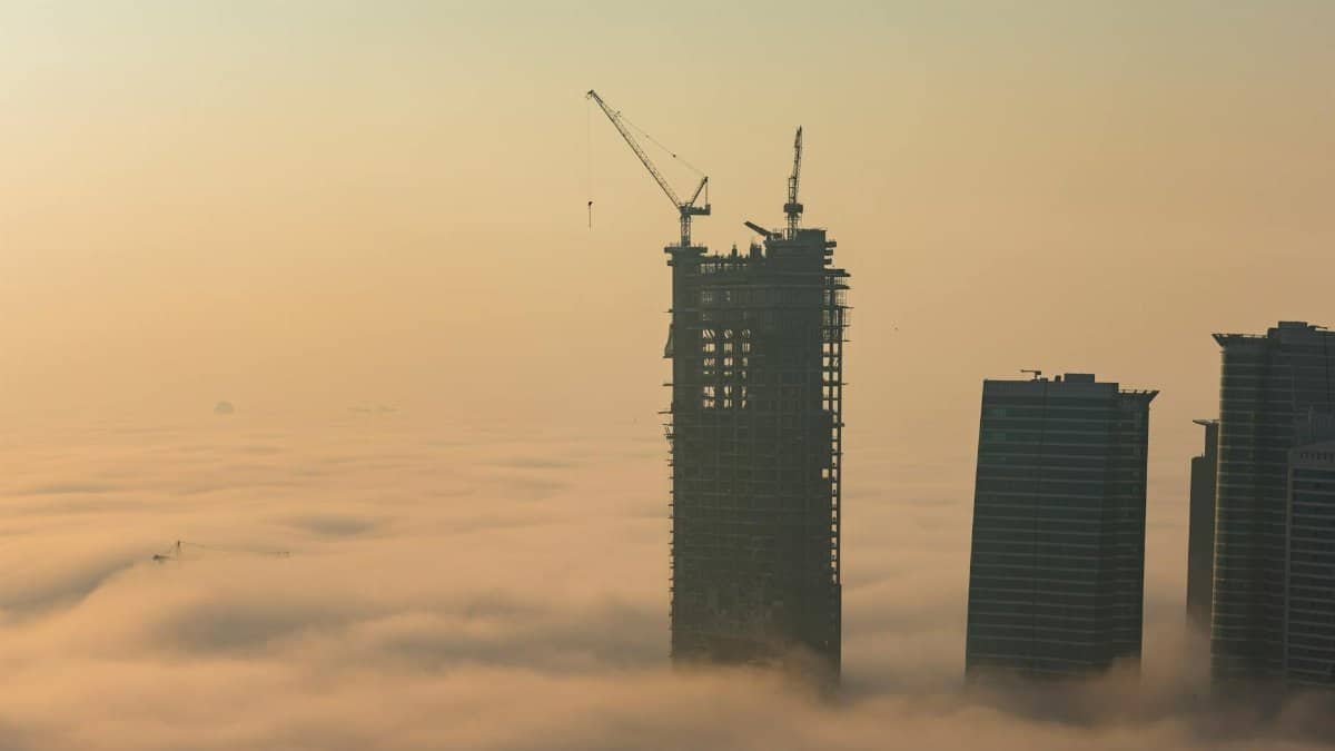 Aerial view of Dubai skyscrapers emerging from thick fog during construction at dawn.
