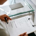 From above of blurred anonymous female psychologist reading documents on clipboard while sitting in office near table during session
