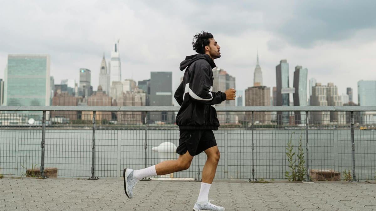 Adult man jogging along a waterfront with the New York City skyline in the background, exuding a vibrant urban lifestyle.