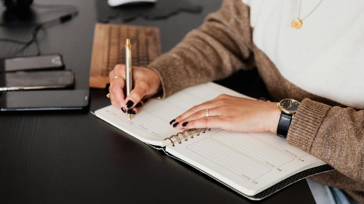 A female freelancer notes plans in a diary at a sleek desk with devices.