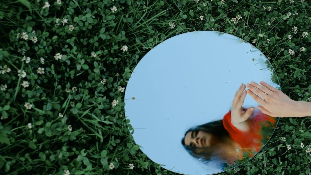 Artistic shot of a woman reflected in a mirror placed on grass, creating a surreal outdoor scene.
