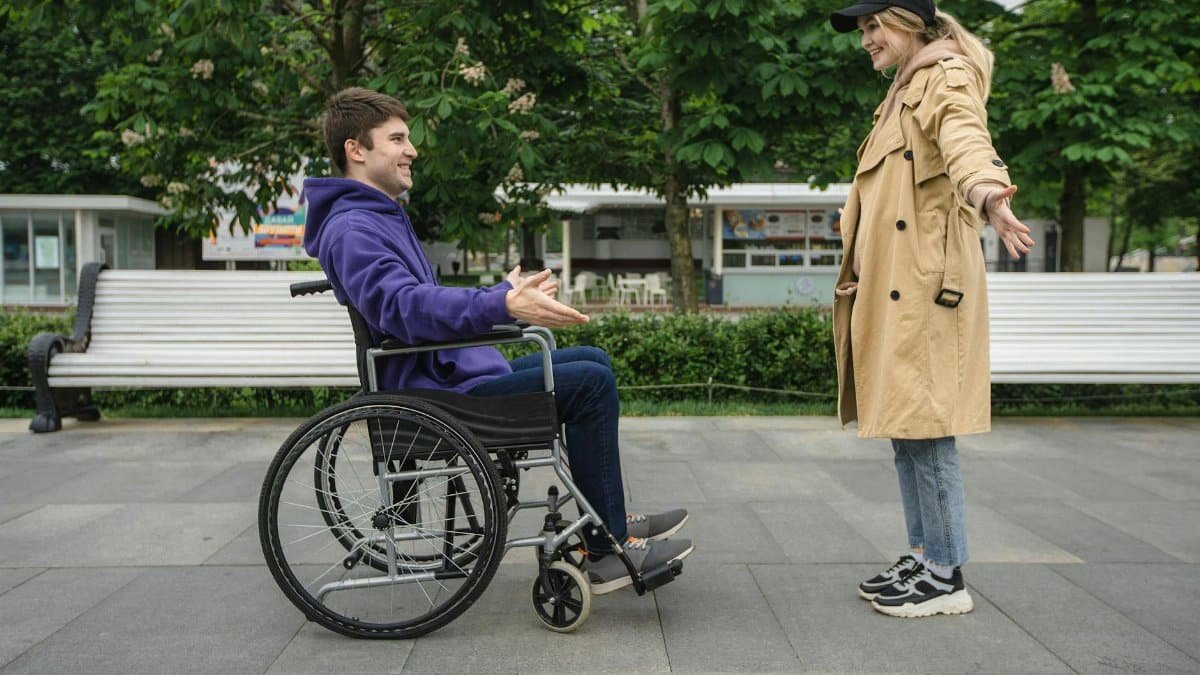 A joyful couple in a park, featuring a man in a wheelchair and a woman in a coat, sharing a moment.