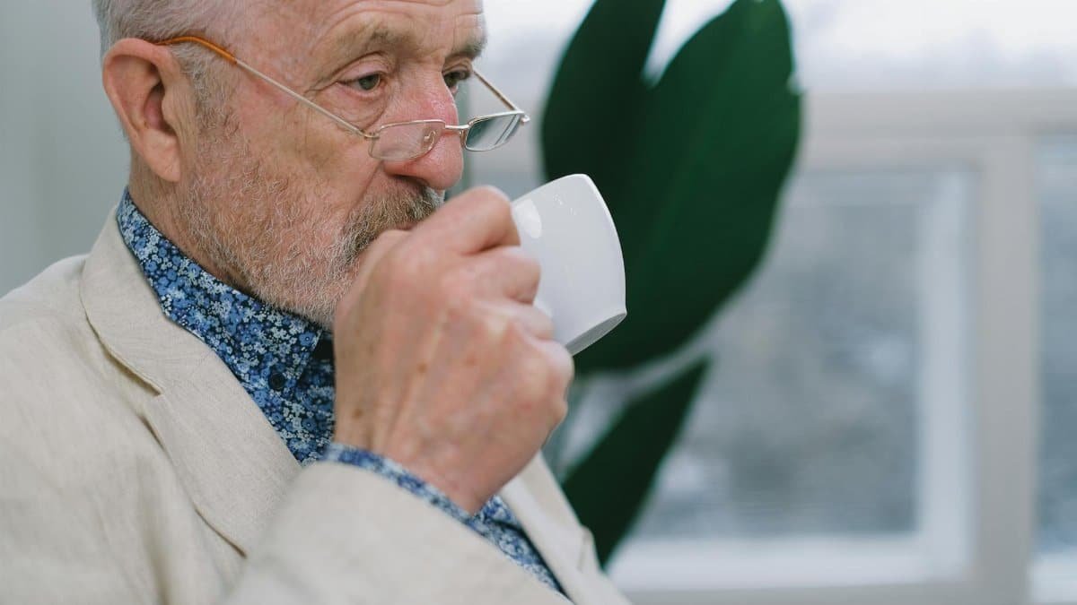 Senior man with eyeglasses enjoying a coffee indoors, conveying a sense of leisure and tranquility.