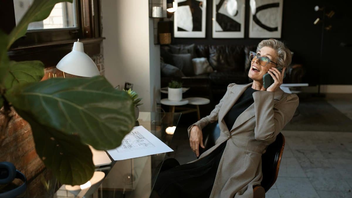 Senior woman in a modern office setting, smiling while on a phone call. Stylish and professional workspace.