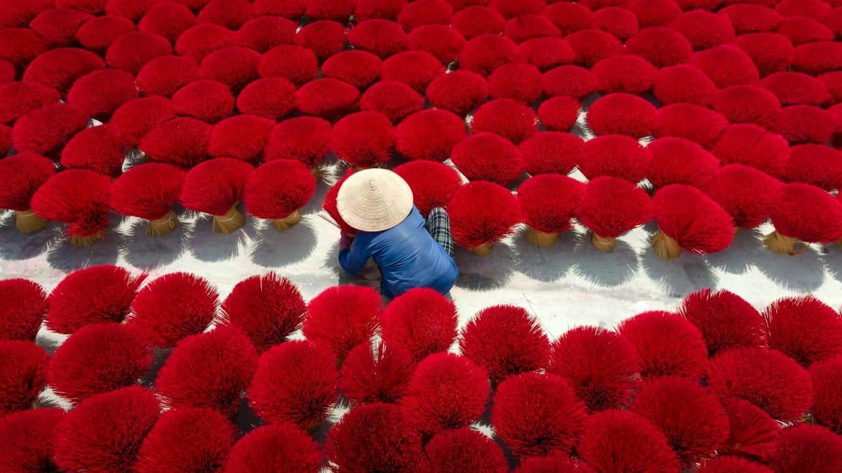 A woman arranges vibrant red incense sticks outdoors in Vietnam.