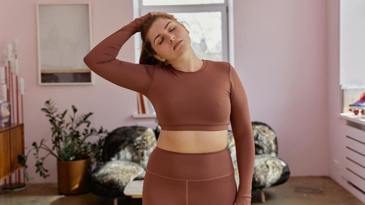 Relaxed plus-size woman in activewear stretching at home, focusing on fitness and wellness.