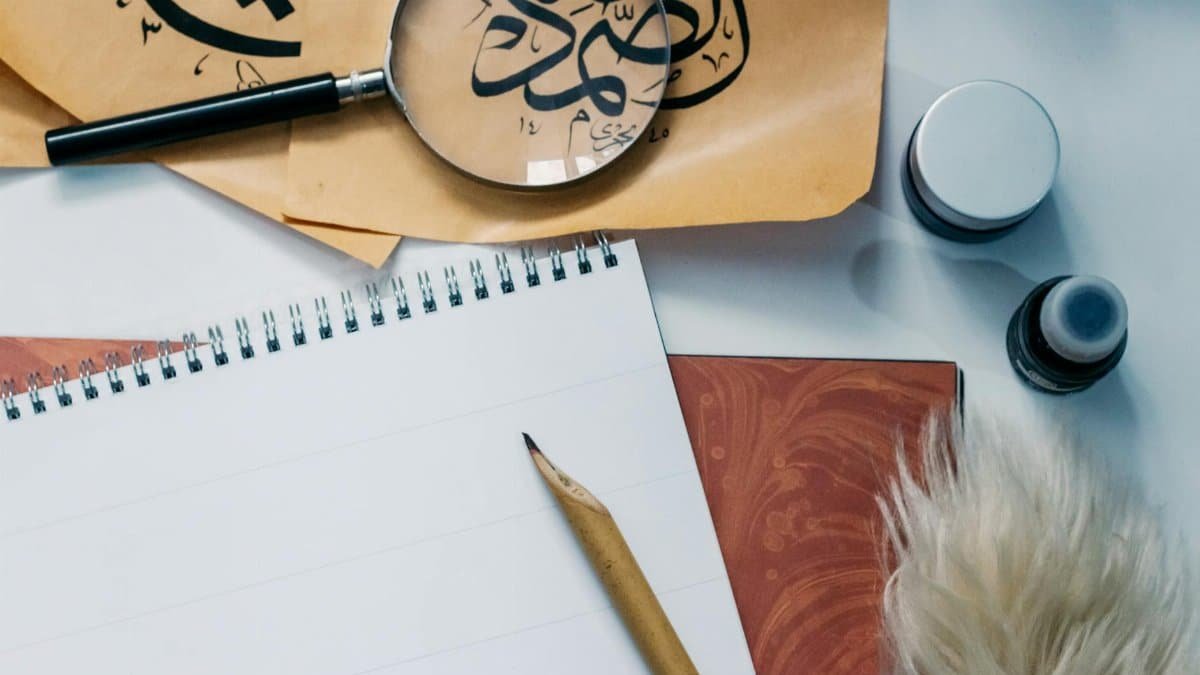Artistic flat lay of calligraphy tools, notepad, and magnifying glass for creative inspiration.