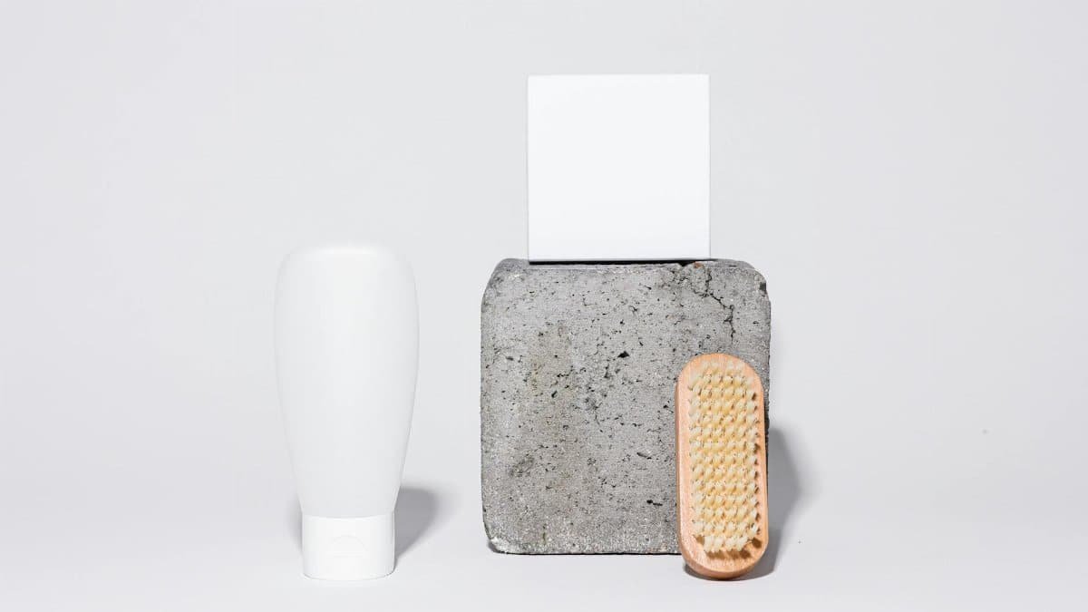 Clean and minimalistic bathroom accessories arrangement featuring a bottle, brush, and stone on a white background.