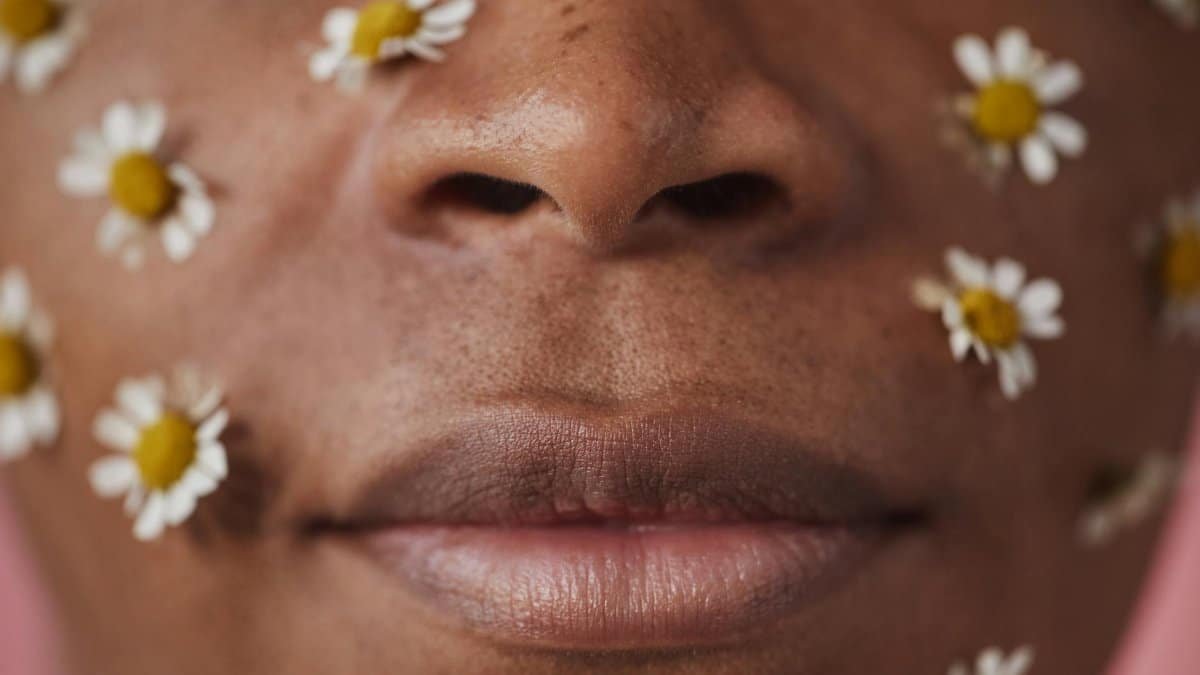 An artistic face close-up adorned with white flowers on a warm-toned skin backdrop.