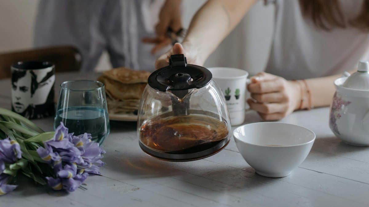 A serene morning breakfast scene featuring a coffee pot, pancakes, and flowers on a table.