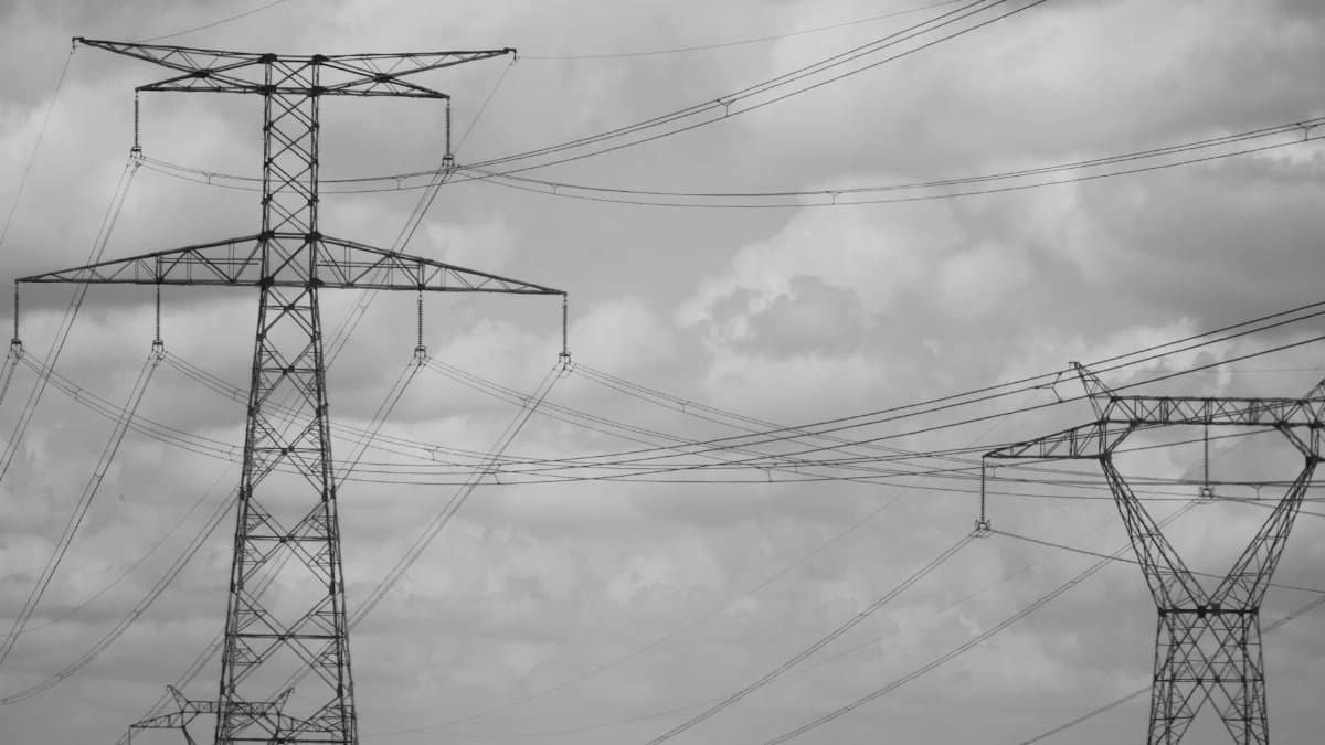 Dramatic black and white photo of high voltage power lines in the sky, showcasing industrial steel structures.