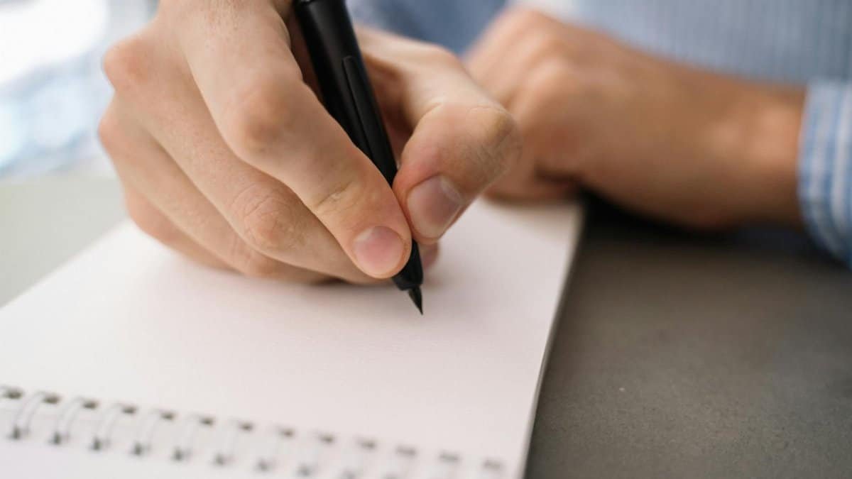 Detailed image of a hand writing with a pen on a spiral notebook, focusing on daily tasks.
