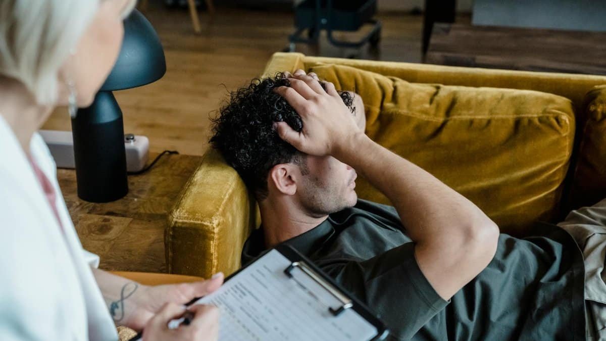 A man lying on a sofa during a therapy session, appearing distressed.