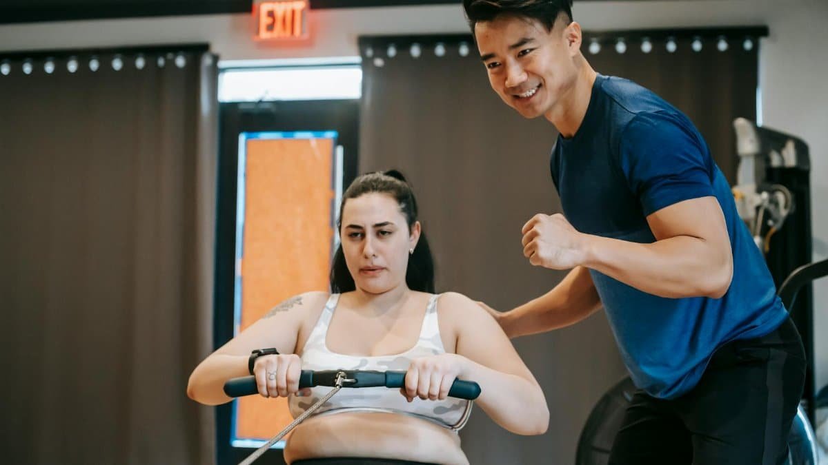 Trainer guides client on rowing machine for intense fitness session in gym.