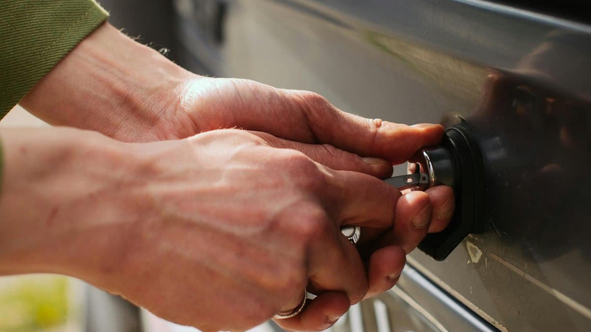 Close-up of hands unlocking a vehicle trunk with a key, showing detail and reflection.