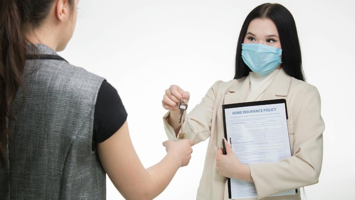 Real estate agent in a face mask hands keys to a client, illustrating safe business practices.
