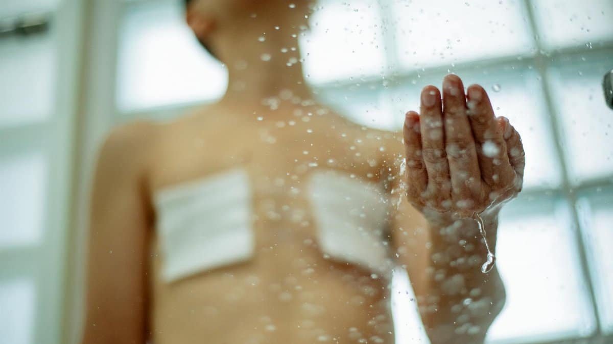 A person with bandages and scars in the shower, illustrating self-care and recovery.