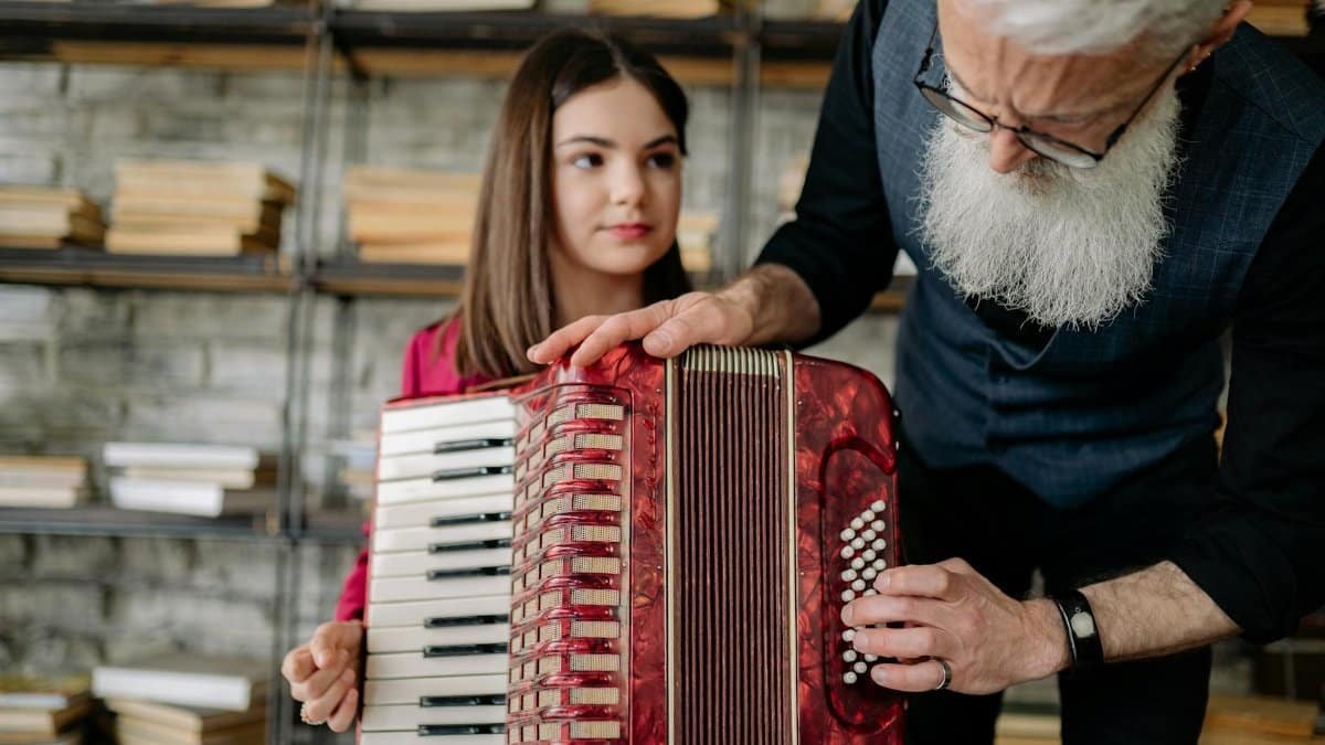 An elderly man instructing a teenage girl on playing an accordion. Perfect for education or music themes.
