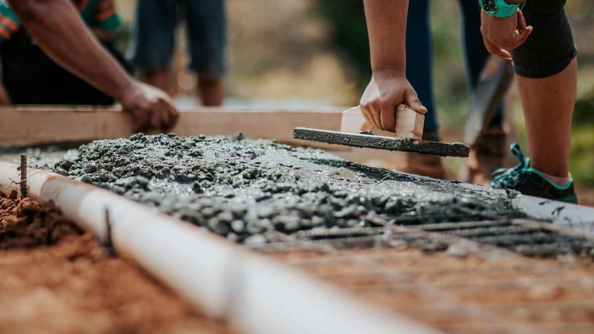 Construction workers leveling fresh cement on a sunny day at an outdoor site.