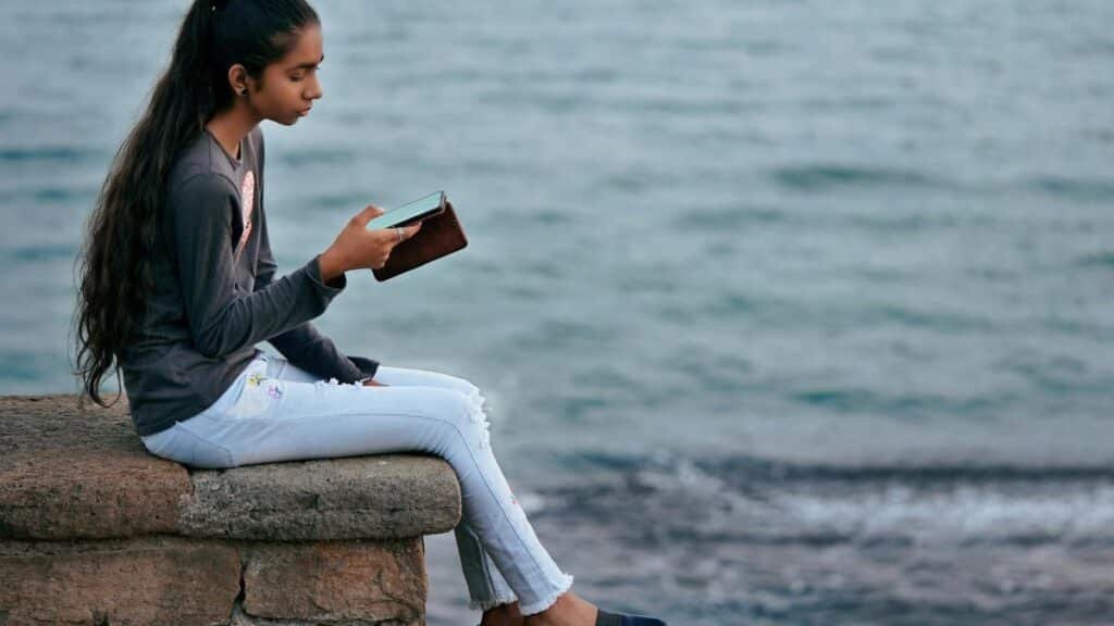 A young woman enjoys a peaceful moment by the sea, engrossed in her smartphone at Diu, India.
